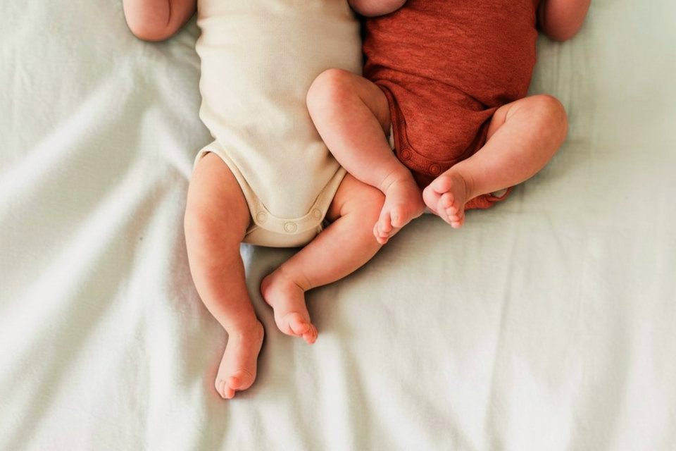 Zwei Babys liegen nebeneinander auf einer weichen weißen Decke